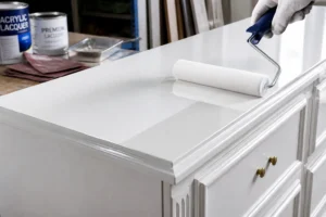 Meuble en bois en cours de peinture blanche laquée avec un rouleau mousse dans un atelier