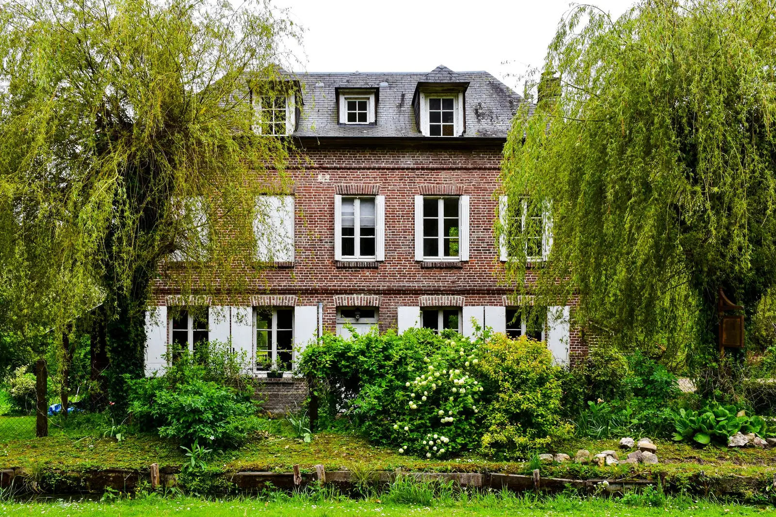 Une maison de briques et son jardin, un saule au premier plan