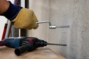 Vissage d'un tirefond béton dans un mur avec une clé à pipe sur chantier