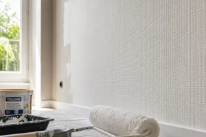 Mur recouvert de toile de verre texturée en cours de rénovation avec rouleau de peinture